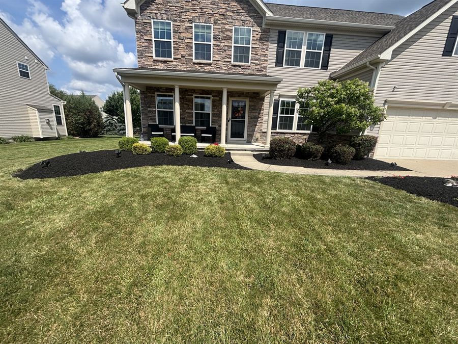 Fresh mowing stripes across a front lawn up to a stone and siding house