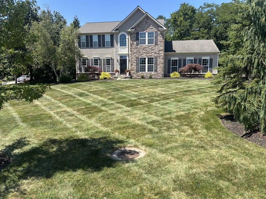 Fresh mowing stripes across the front lawn of a stone-front house